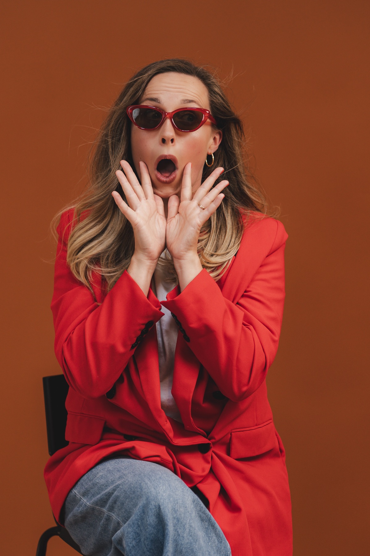 Jasmine in a red blazer and sunglasses against a warm terracotta backdrop