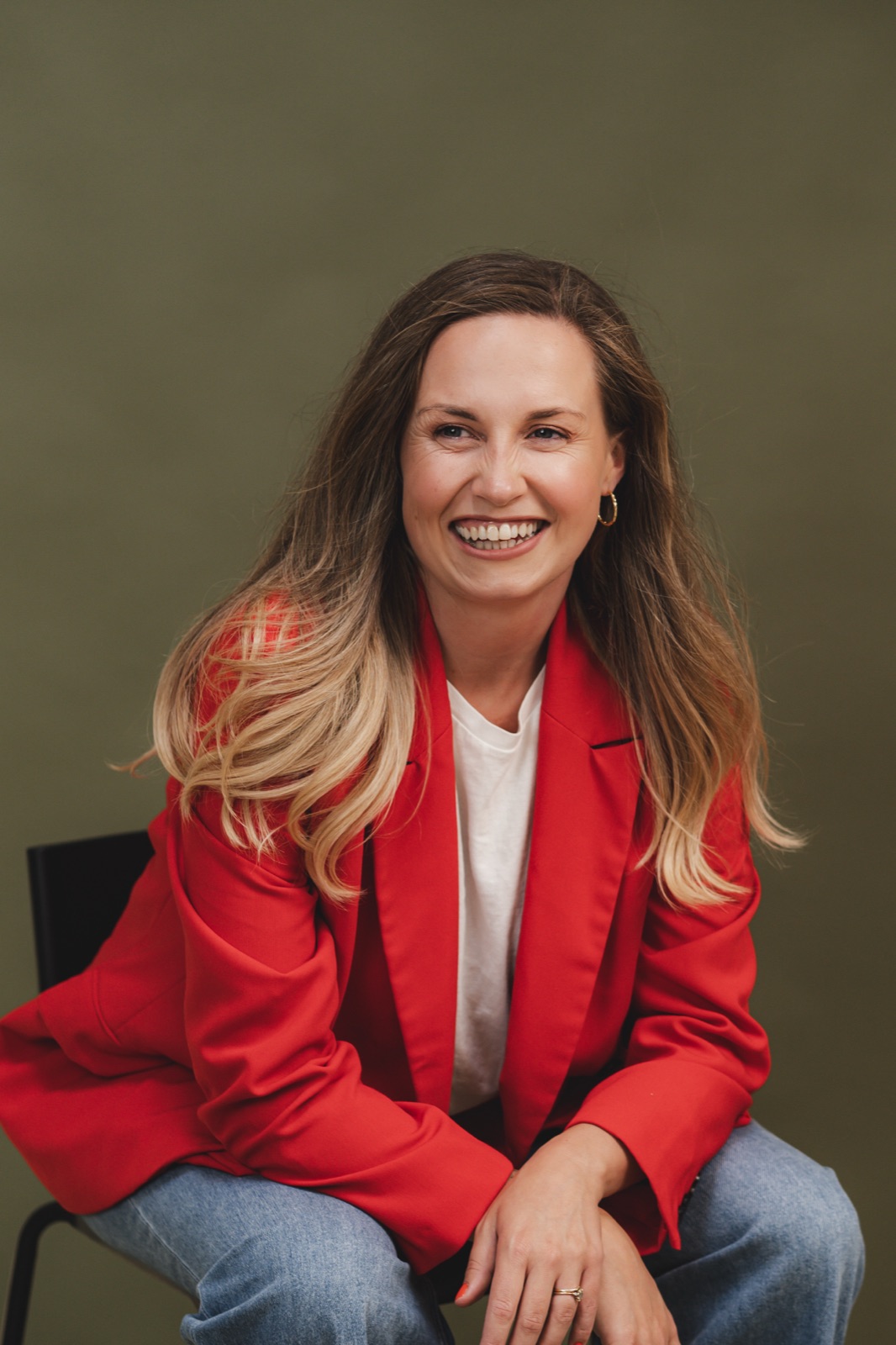 Jasmine laughing in a red blazer against a green backdrop